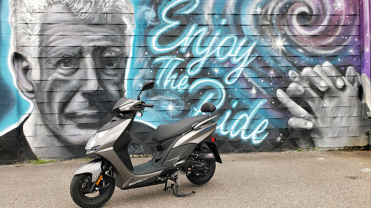 A scooter parked in front of a wall with graffiti.