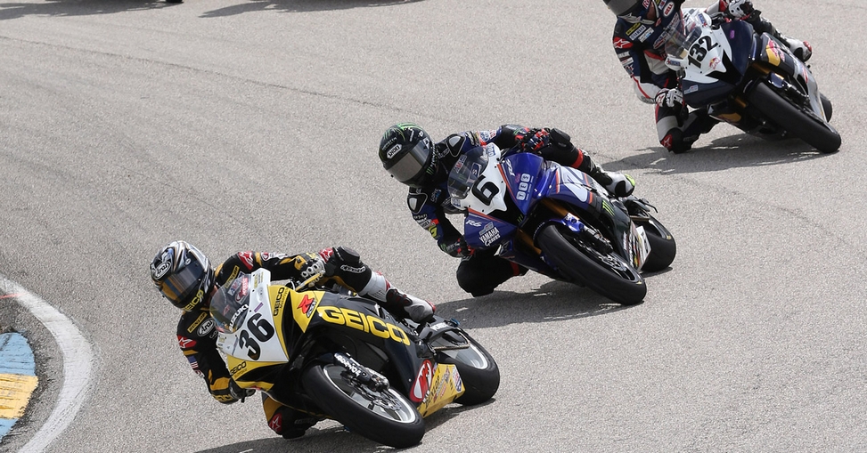 Two motorcycles racing on a track with people watching.